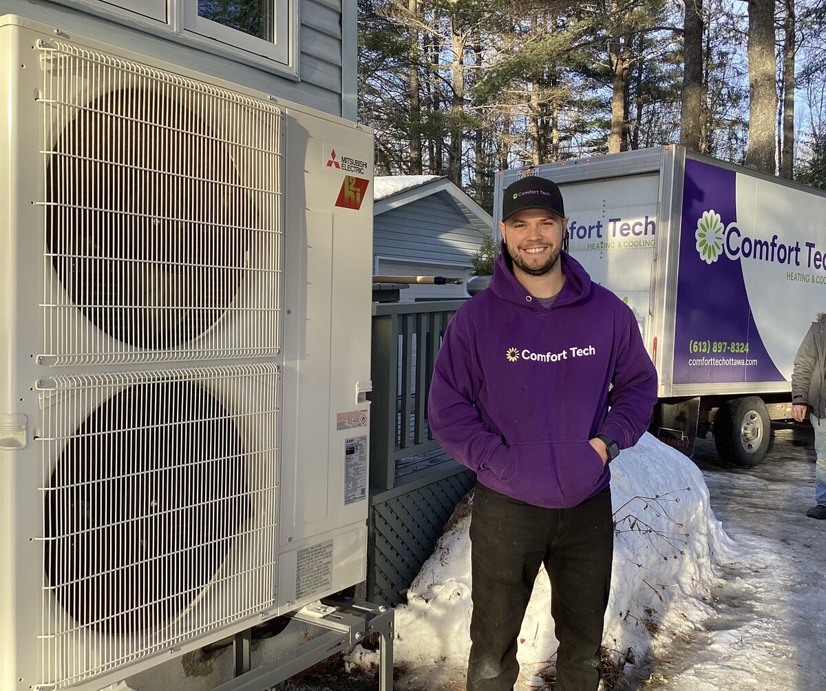 Comfort Tech installer standing next to Mitsubishi h2i heat pump in winter with branded truck